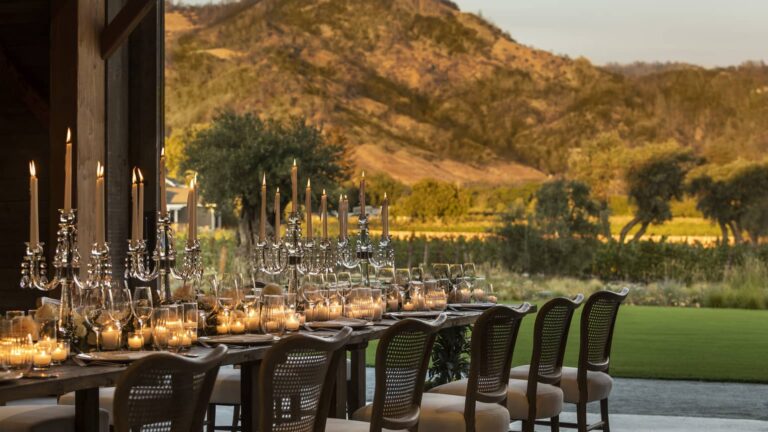 Elegant outdoor dining setup with candlelight and long table overlooking scenic landscape at sunset